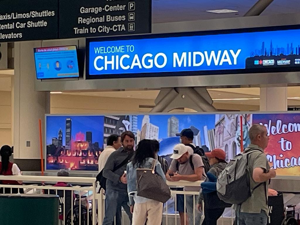Travelers in the arrivals hall at Chicago Midway International Airport beneath the Welcome to Chicago Midway sign