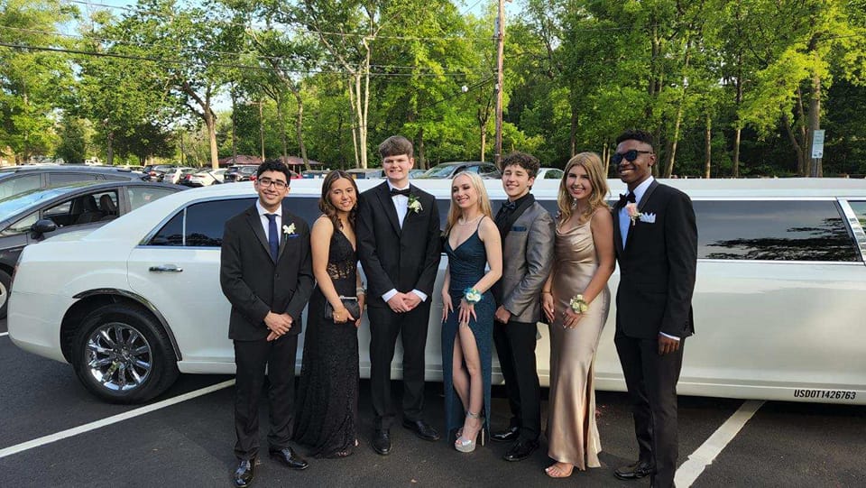 Group of friends standing in front of a stretch limousine, dressed in formal attire for prom night.